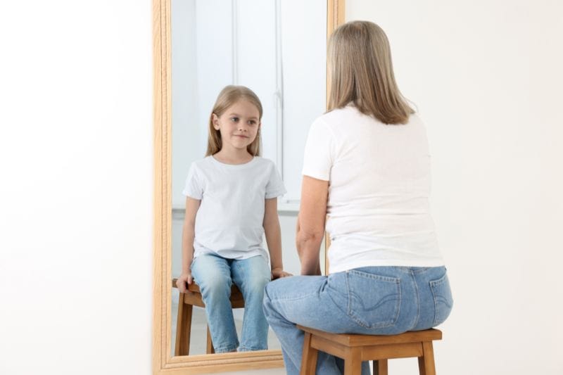 Frau schaut in den Spiegel und sieht sich selbst als kleines Kind. Inneres Kind heilen und Groll loslassen.