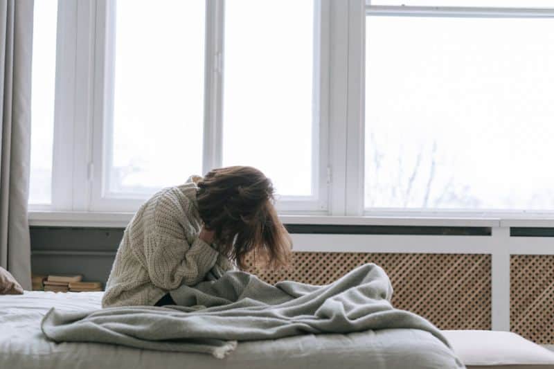 Frau liegt sitzt auf ihrem Bett und ist verzweifelt und traurig – Symbol für den Schmerz nach einer zerbrochenen Freundschaft